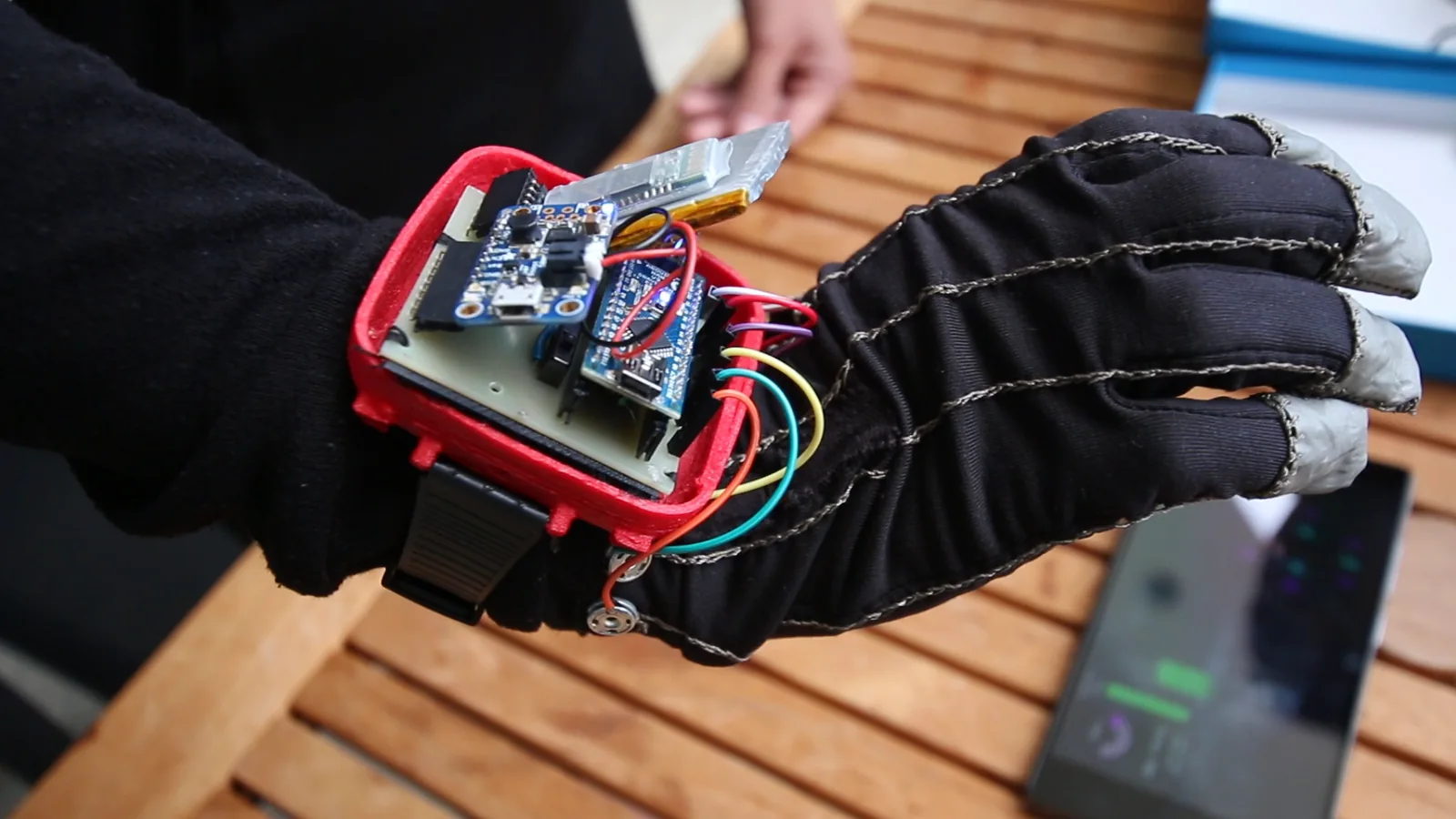 A wired sensor glove with an open red wrist case showing its circuit boards, on a table at a 2018 conference.